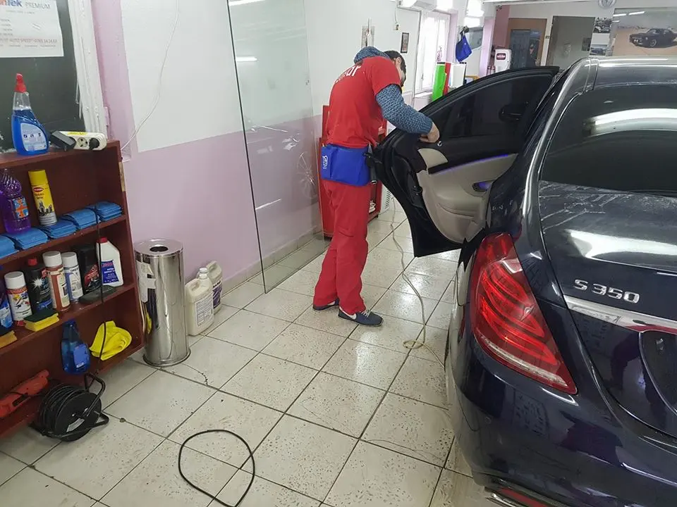 Tehnician montând folie pe geamul din spate al unui Mercedes S350, în atelier