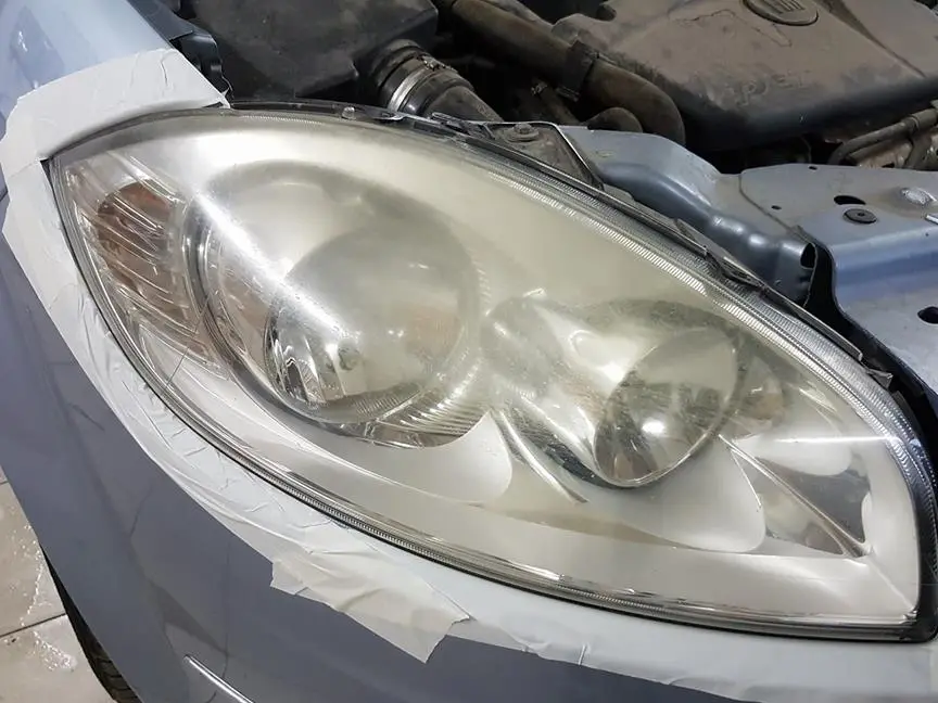 Far de Peugeot îngălbenit și mătuit, cu caroseria protejată cu bandă, înainte de polish